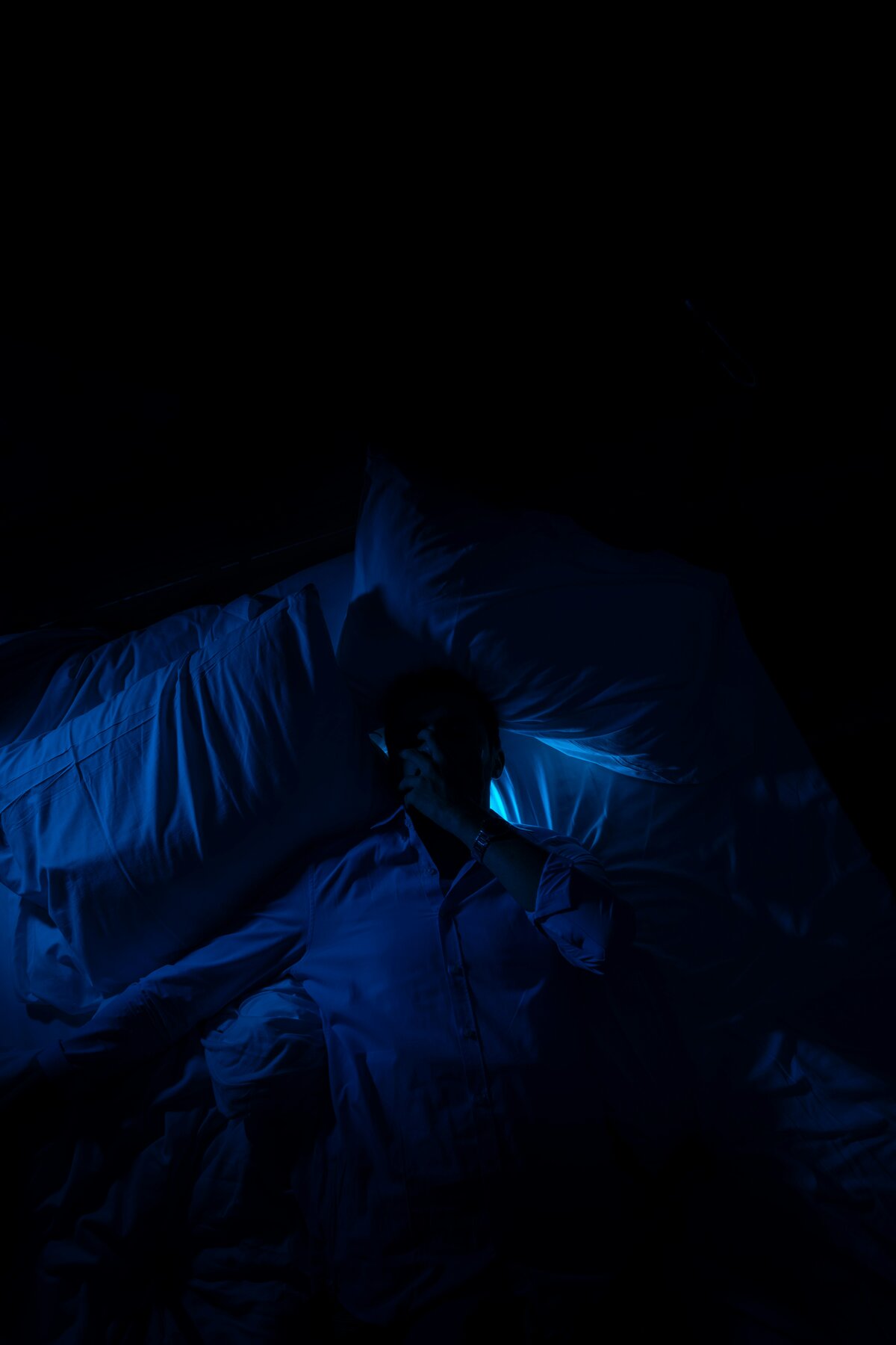 Person sitting on the edge of a bed at night unable to sleep due to frequent urination
